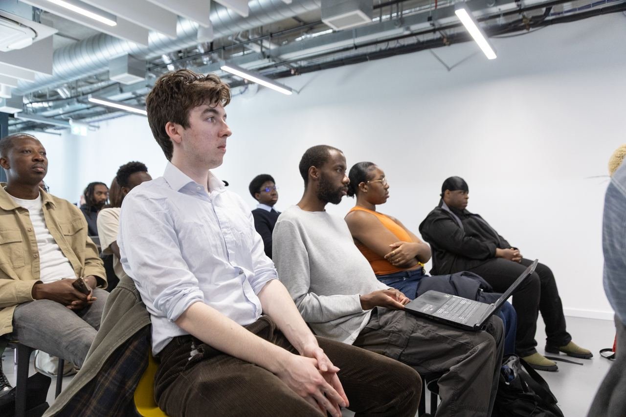 Students seated with laptops, focused on a presentation.