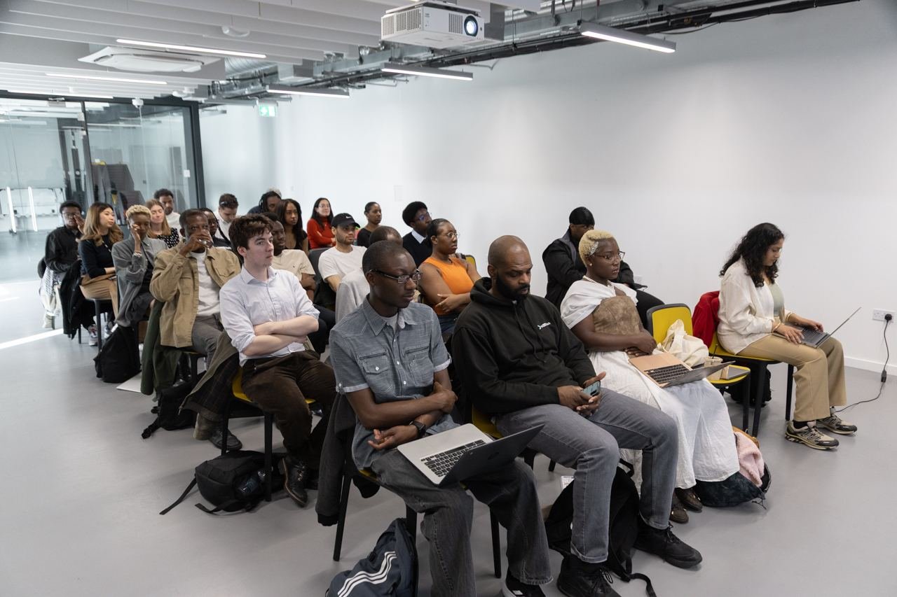 A full room of students seated on rows of chairs, laptops open, listening to a session.