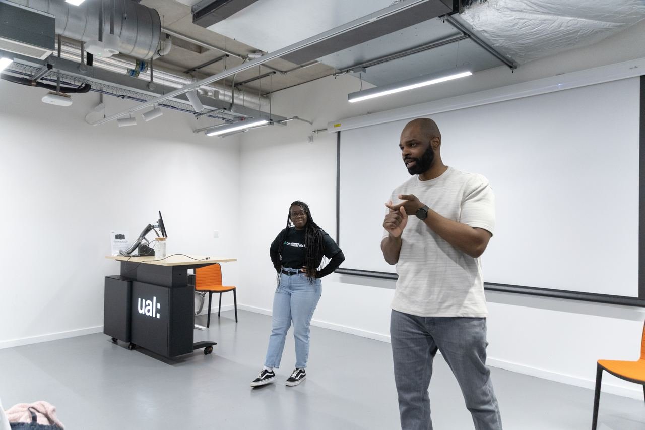 A speaker addresses the room at a Peckham DAZ session, with a UKBlackTech team member standing by the UAL podium.